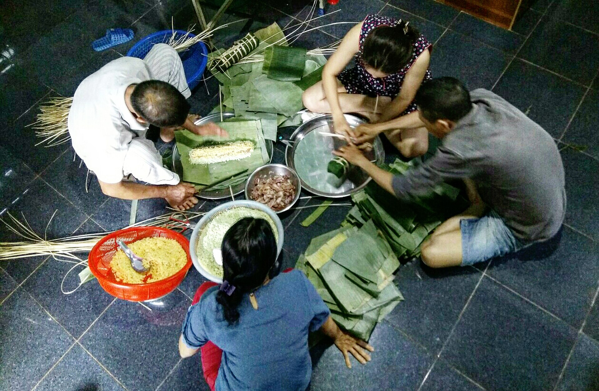 People sitting on the floor cooking and wrapping food together