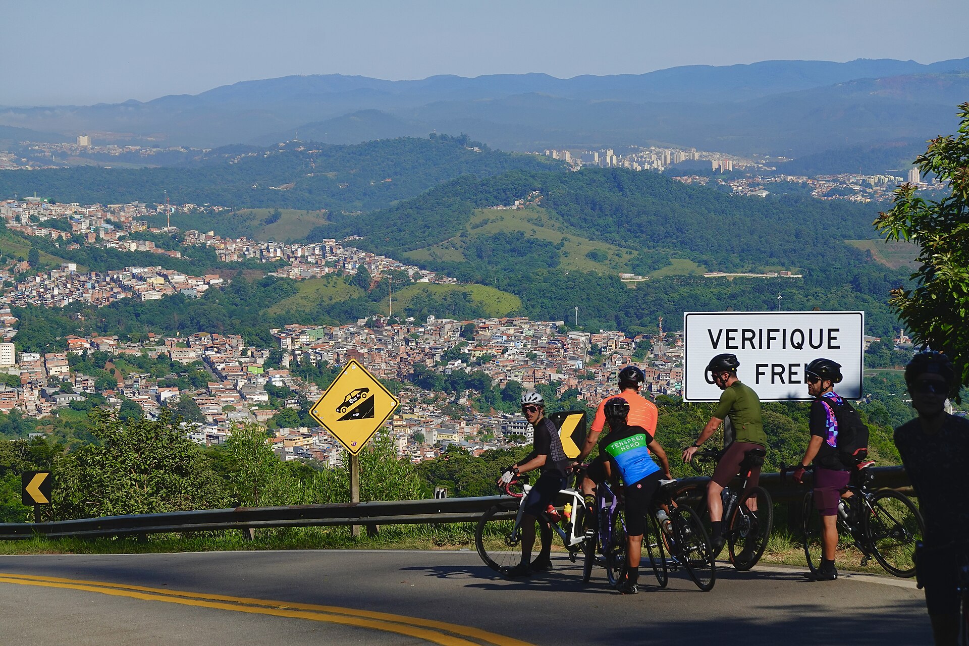 A group of cyclists resting with their bikes on a road overlooking the city