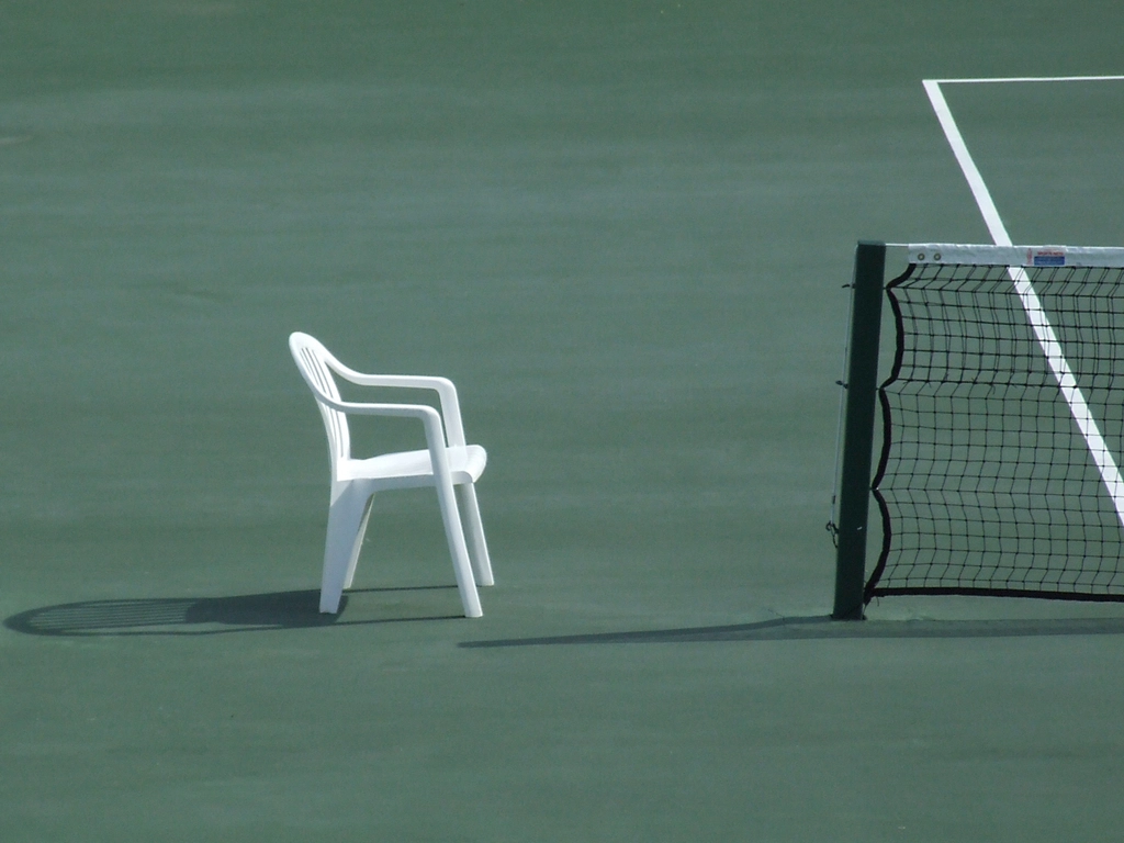 An empty tennis court with a net and a chair in the sun